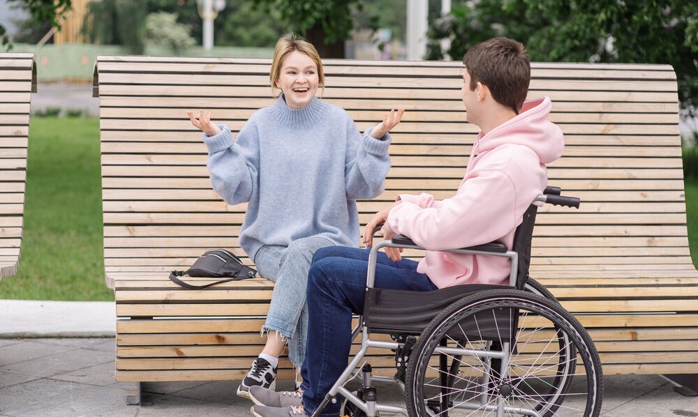 Eine junge Frau sitzt auf einer Bank und spricht angeregt mit einem jungen Mann im Rollstuhl. | © Pexels / Shvets Production