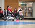 Das Team mit rot-weissen Leibchen spielt Powerchair-Hockey im Rollstuhl. Sie befinden sich in einer Halle. | © PCH Worldcup