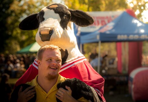 Un humain atteint de trisomie 21 est étreint par derrière par une vache en peluche. | © unsplash